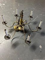 Top-down view of the brass chandelier with six arms and candle-style sockets on a grey floor.