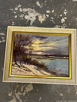Framed oil on board painting showing snowy lakeside landscape with sunset sky, signed Lyon in bottom left corner.