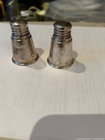 Front view of two tapered sterling silver salt and pepper shakers with ridged tops and multiple holes for dispensing seasoning, showing surface wear and tarnishing.