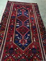 Full view of Persian wool rug showing geometric medallion and border designs in red, navy, and other colors.