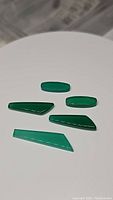 Photo of five polished green onyx gemstones in various elongated and trapezoidal fancy cuts laid on a white surface.