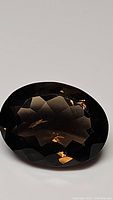 Close-up photo of a large, oval shaped faceted smokey quartz gemstone showing dark brown color and internal light reflections.