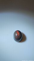 Photo of 1.42ct natural oval Ethiopian black opal on white background showing red color flash.