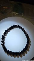 Photo of a circular stretchy bracelet made of shiny round black onyx beads laid flat on a white surface.