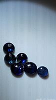 Six natural blue sapphire round cabochon gemstones displayed on flat surface showing their color, shape, and transparent qualities.