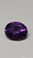Top view of oval cut deep purple amethyst gemstone showing facets and rich color.