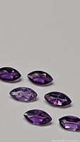 Six marquise cut deep purple amethyst gemstones laid out on white background, showing upper polished faceted surface and consistent calibration size.