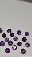 Multiple round cut purple amethyst gemstones showing various shades of purple, arranged on a white background.
