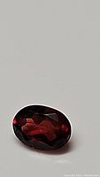 Close-up photo of a deep cherry red oval cut garnet gemstone showing facets and light reflection.
