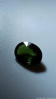 Close-up of oval cut chrome tourmaline gemstone reflecting green hues and light.