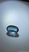 Top view of the oval cut deep blue aquamarine gemstone showing facets and color.