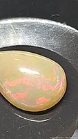 Close-up of the teardrop-shaped Ethiopian opal showing light chocolate base color with bright red and pink play of color.