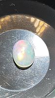 Close up image of an oval cabochon opal showing multicolor rolling flashes on a reflective metal surface.