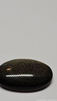 Oval cabochon gold sheen obsidian gemstone with visible golden sparkles under ambient light on a white background.