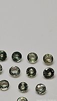 Photo showing multiple small round cut natural green sapphires laid out on a plain background, displaying their size, shape, and color.