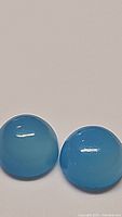 Pair of round, bright icey blue chalcedony cabochon stones placed side by side, showing color and smooth curved surface.