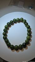 Photo of a stretchy bracelet made of round polished natural green jade beads laid flat on a white surface.