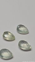 Four pear-shaped mossy green prehnite gemstones with checkerboard cuts, displayed on a neutral background.