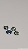 Four oval rose cut natural sapphires showing multicolored hues including blue, green, and yellow tones on a white background.