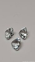 Three natural Trillion cut Aquamarine/Goshenite gemstones shown against gray background with good focus and lighting highlighting the gemstone facets and clarity.