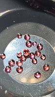 Photo showing multiple small round cabochon garnet gemstones with vibrant red color scattered on a reflective black surface.