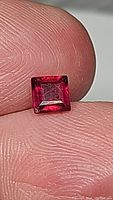 Close-up of the square cut natural ruby held between fingers showing its blood red color and facets.