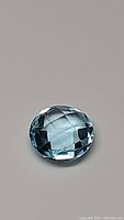 Clear close-up image of a natural Swiss blue topaz gemstone with a round checkerboard cut and brilliant lagoon blue color showing facets and high clarity.