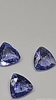 Close-up photo of three trillion cut blue purple tanzanite gemstones showcasing their color and clarity.