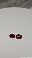 Pair of deep red oval cabochon carnelian gemstones on white background, showing shape and color