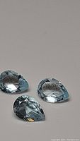 Three pear-shaped natural sky blue topaz gemstones laid on a plain surface, showing color, cut and clarity.