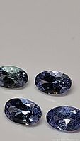 Four oval cut tanzanite gemstones arranged on a plain light surface, showing color and clarity under light.