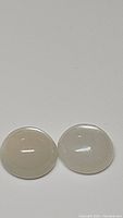 Pair of round cabochon white moonstones showing translucent white body and flash.