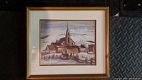 Framed print showing a winter landscape with a church and snow-covered ground under a muted sky.