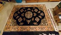 Rectangular Asian style area rug with black central field and decorative peach border, floral and geometric motifs, laid out on floor