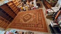 Photograph of the traditional patterned area rug laid on floor surrounded by bookshelves and boxes.