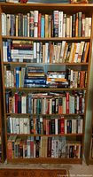 Photo of a wooden bookshelf filled with several rows of books in various sizes and colors.