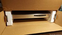 Range hood partially visible inside original cardboard box showing stainless steel finish and control panel.