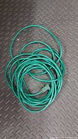Photo shows a coiled green extension cord with 3-prong plug and receptacle on ends, laid on textured black surface.