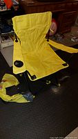 Yellow fold-up lawn chair set up with armrests and cup holder, yellow carry bag placed on floor beside it.