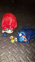 Two drawstring bags, one red and one blue, placed on a textured dark surface with various glass marbles scattered around them.