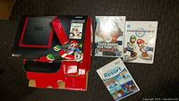 Red and black Nintendo Wii Mini box with 4 Wii games displayed next to it: Tiger Woods PGA Tour 09, Mario Kart Wii, Wii Sports Resort, Super Mario Bros Wii game disc.