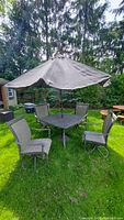 Full view of patio furniture set including table, four chairs, and umbrella on grass lawn