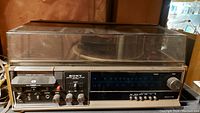 Front view of Sony stereo system showing cassette player, tuner dial, and control knobs with clear plastic dust cover
