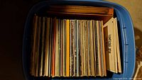 Top-down view of a blue bin filled with many vinyl records packed vertically revealing thickness and spines