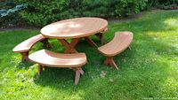 Wooden outdoor patio furniture set on grass including round table with umbrella hole and four curved benches.