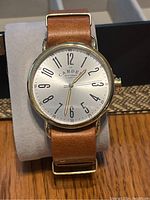 Front-facing photo capturing the entire watch, showing the dial with branding, hands, numerals, leather strap, and case details.