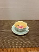 Photo of tea cup set with blue saucer, yellow interior with pink rose floral design, gold trim, scalloped edges