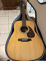 Full view of guitar body inside soft case on tiled floor showing natural wood finish and black pickguard