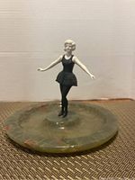 Front view of ballerina figurine on green marble base showing posed arms, black ballet dress and shoes