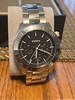 Photo showing the front of a stainless steel Fossil wristwatch with black dial and chronograph subdials on a cushion.